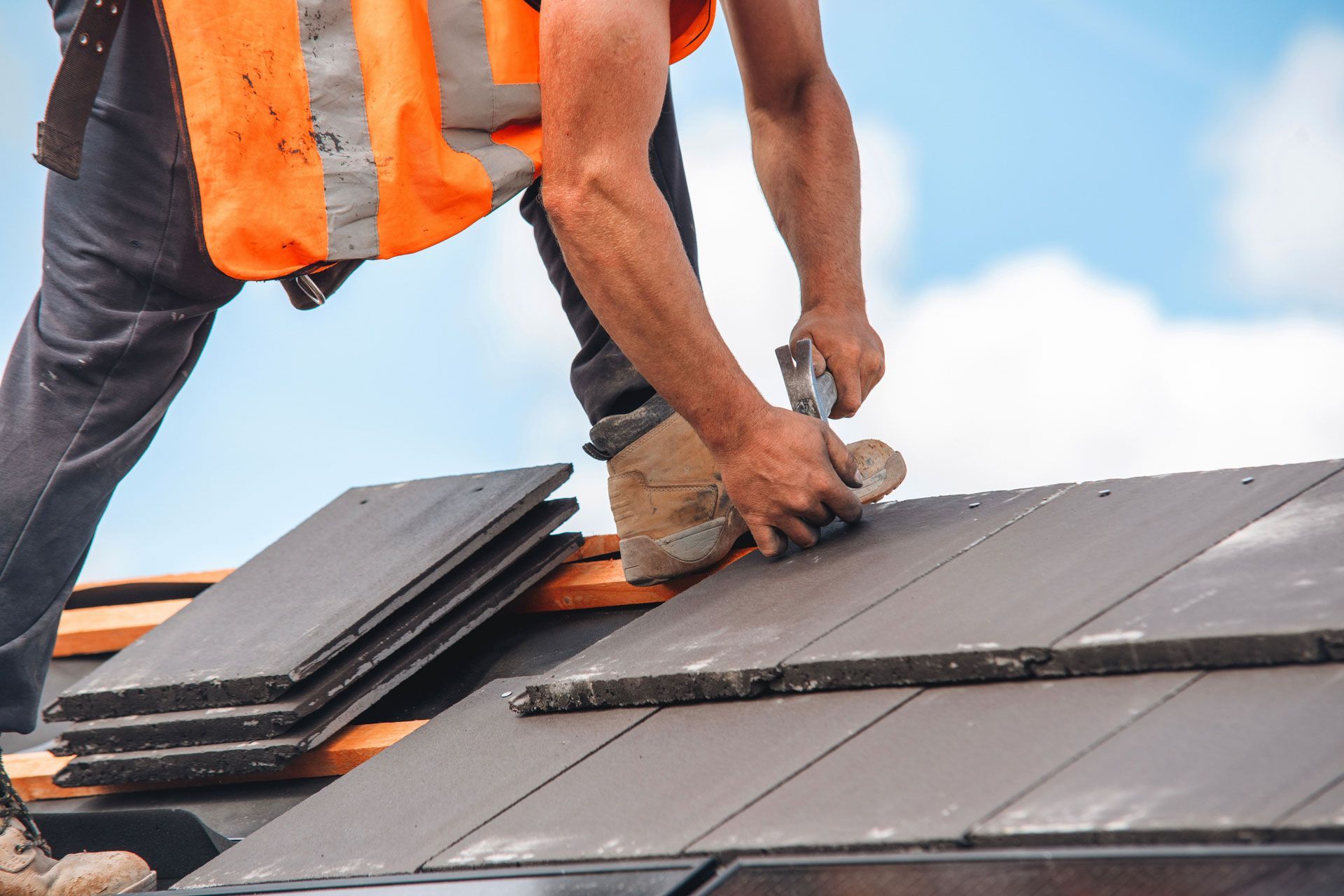 Roofer wearing safety vest working on a roof, installing dark tiles.