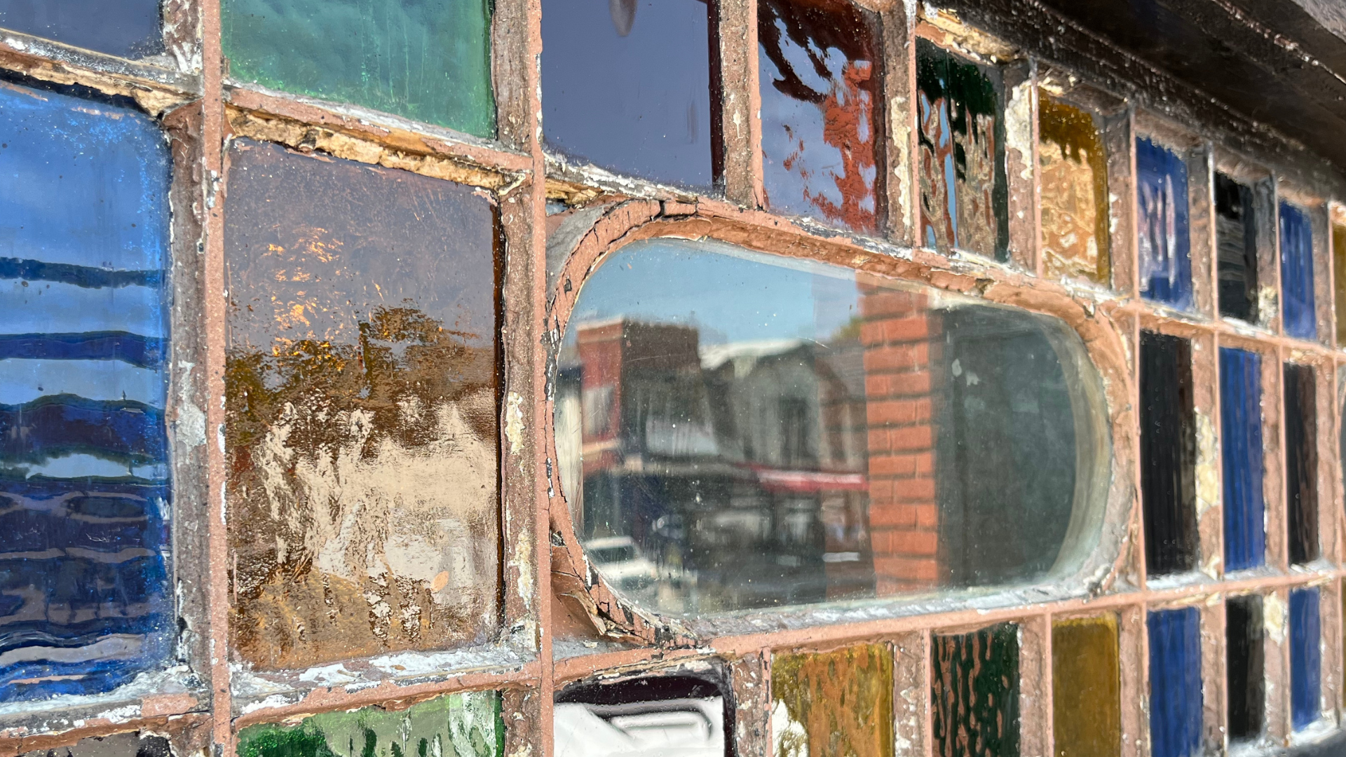 A close up of a stained glass window with a brick building in the background.
