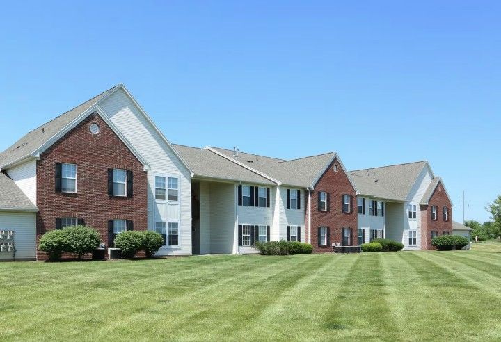 Two-story apartment building with brick and white siding, green lawn, and blue sky.