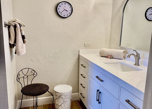 There is a clock on the wall above the sink in the bathroom.