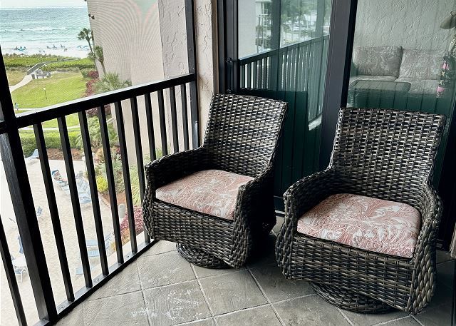 Two wicker chairs are sitting on a balcony overlooking the ocean.