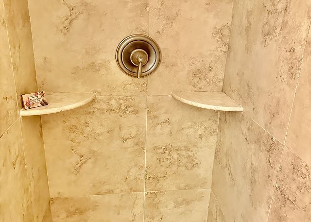 A shower with a shower head and shelves in a bathroom.