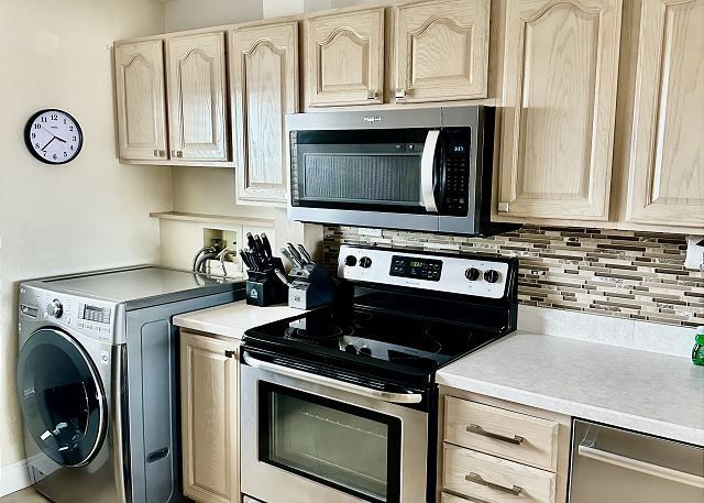 A kitchen with a stove , microwave , washer and dryer.