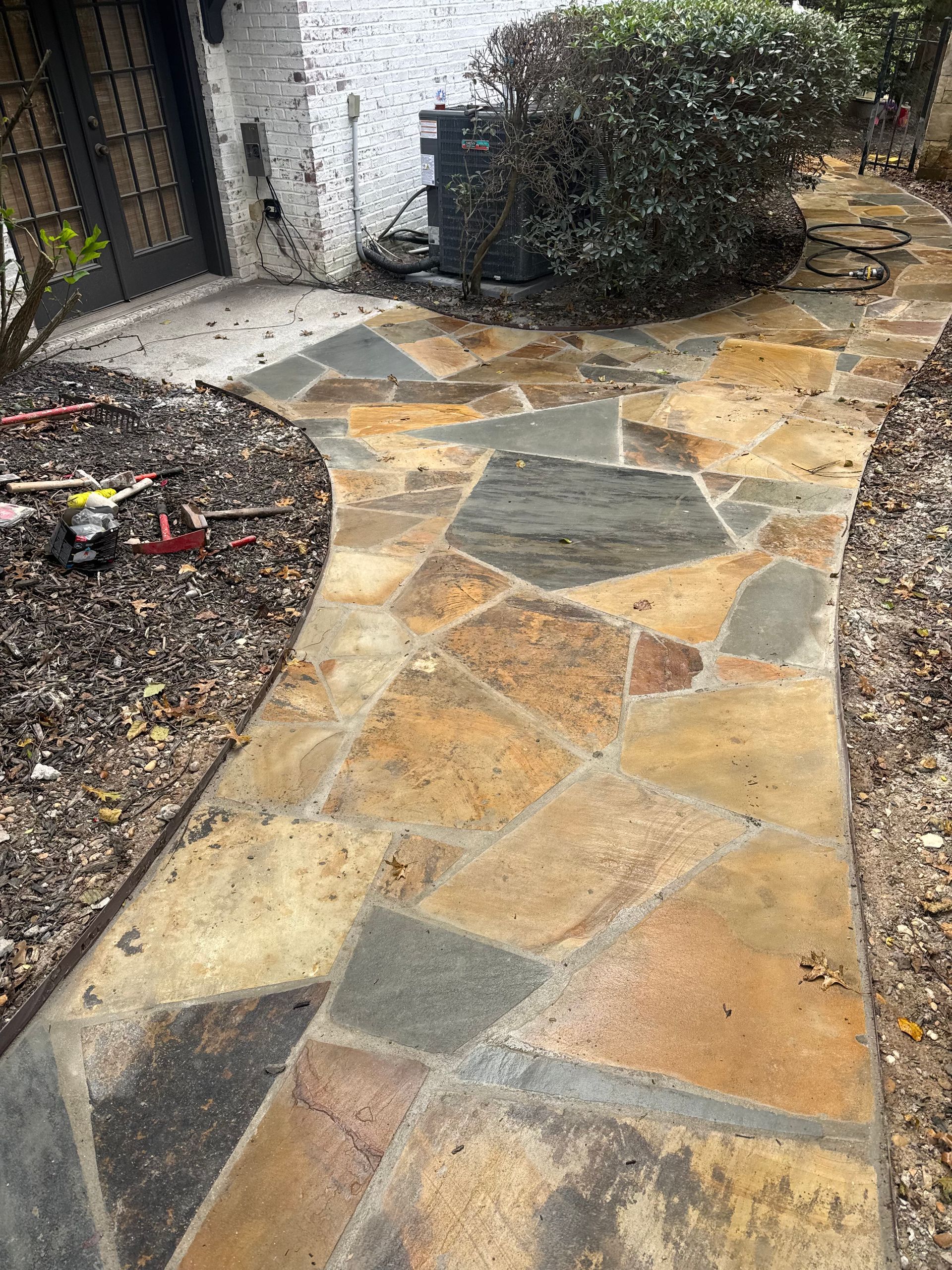 Stone walkway curving past mulch beds and shrubs beside a house entrance
