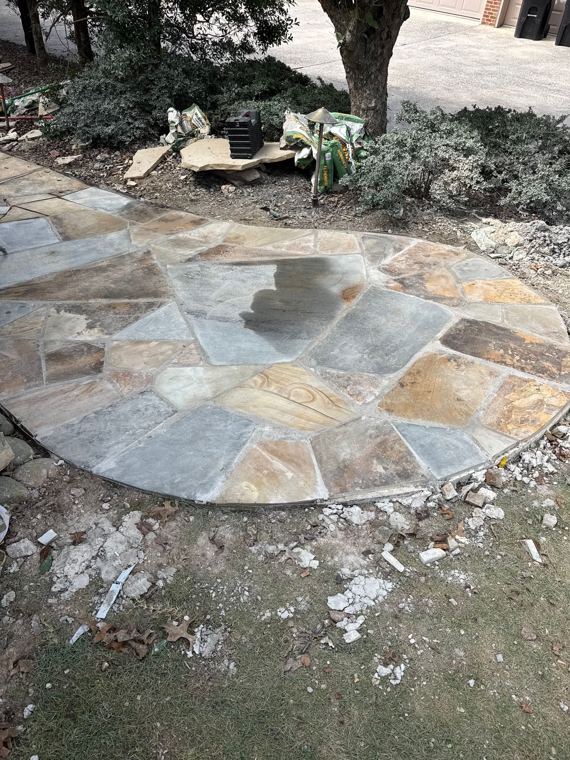 Circular stone patio in a garden with shrubs and a tree nearby