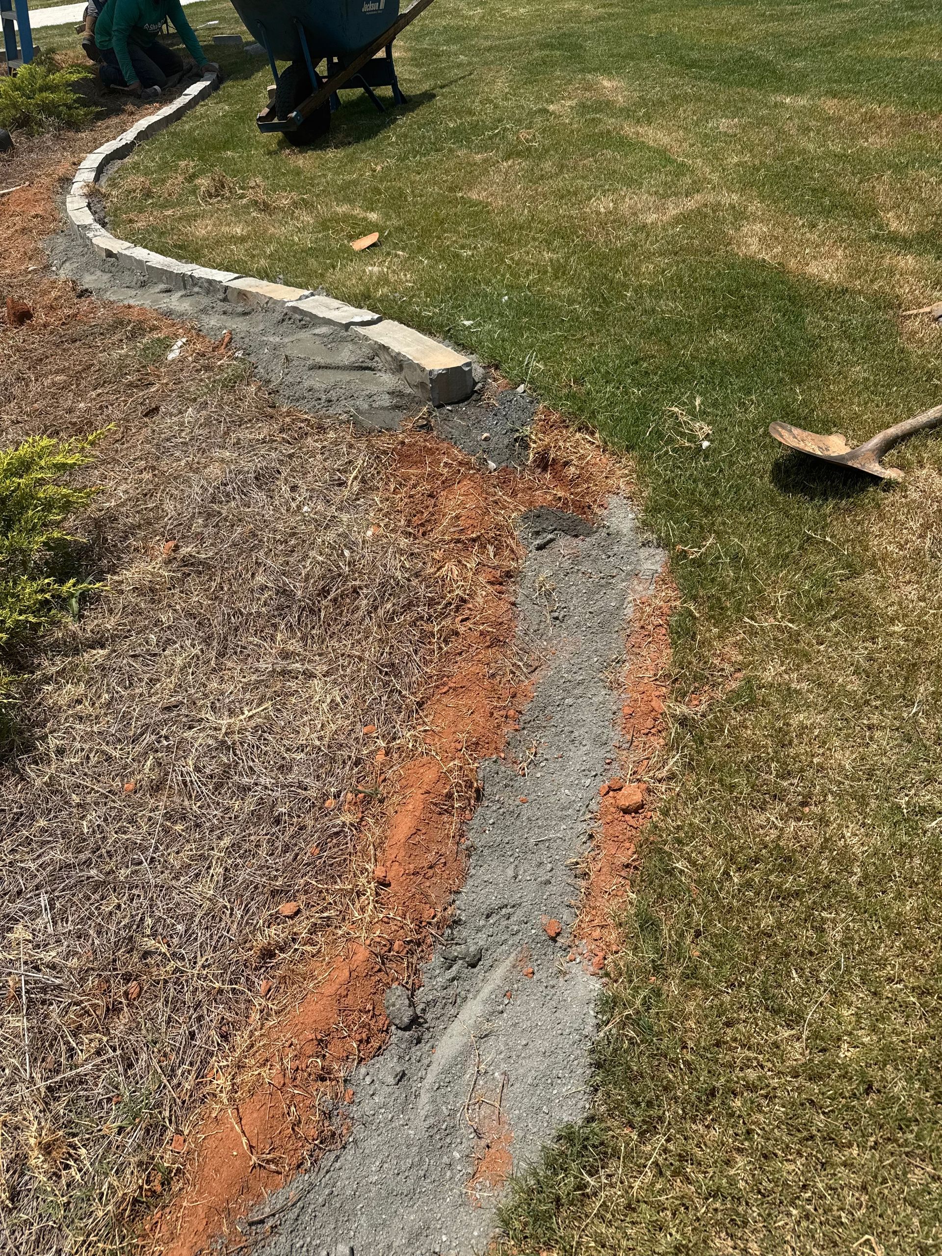 Curved stone border separating gravel and grass, with a rust-colored line along the edge.