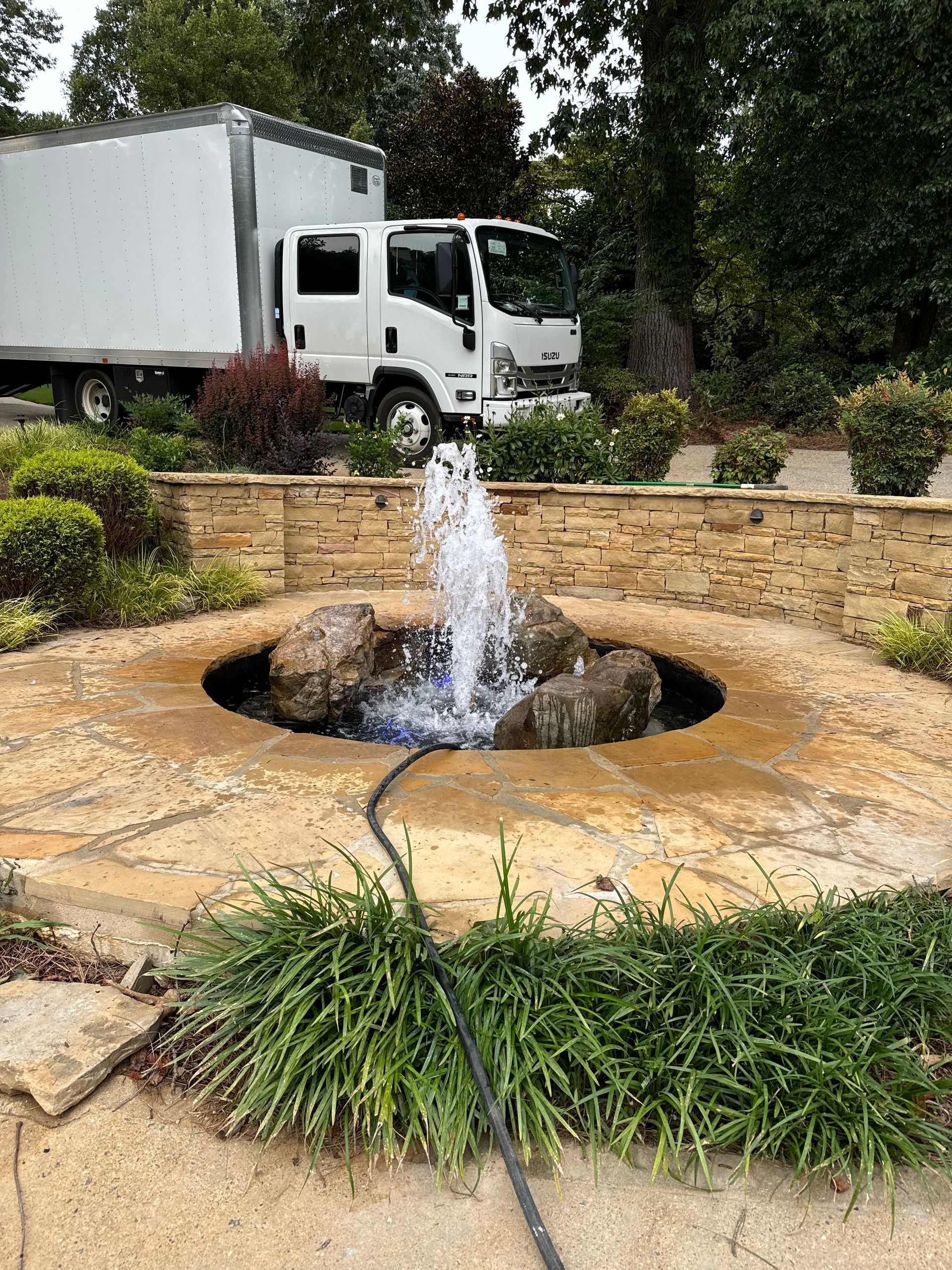White truck by stone fountain with water flowing in a landscaped garden