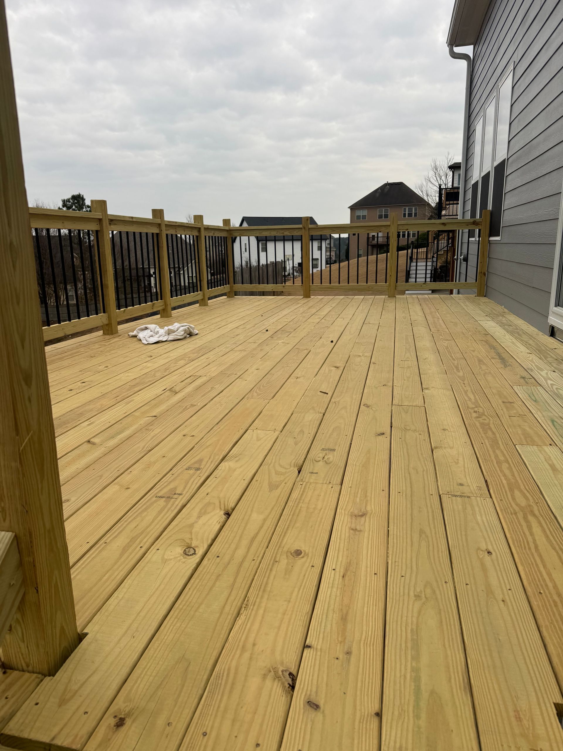 Wooden backyard deck with railings beside a house under a cloudy sky