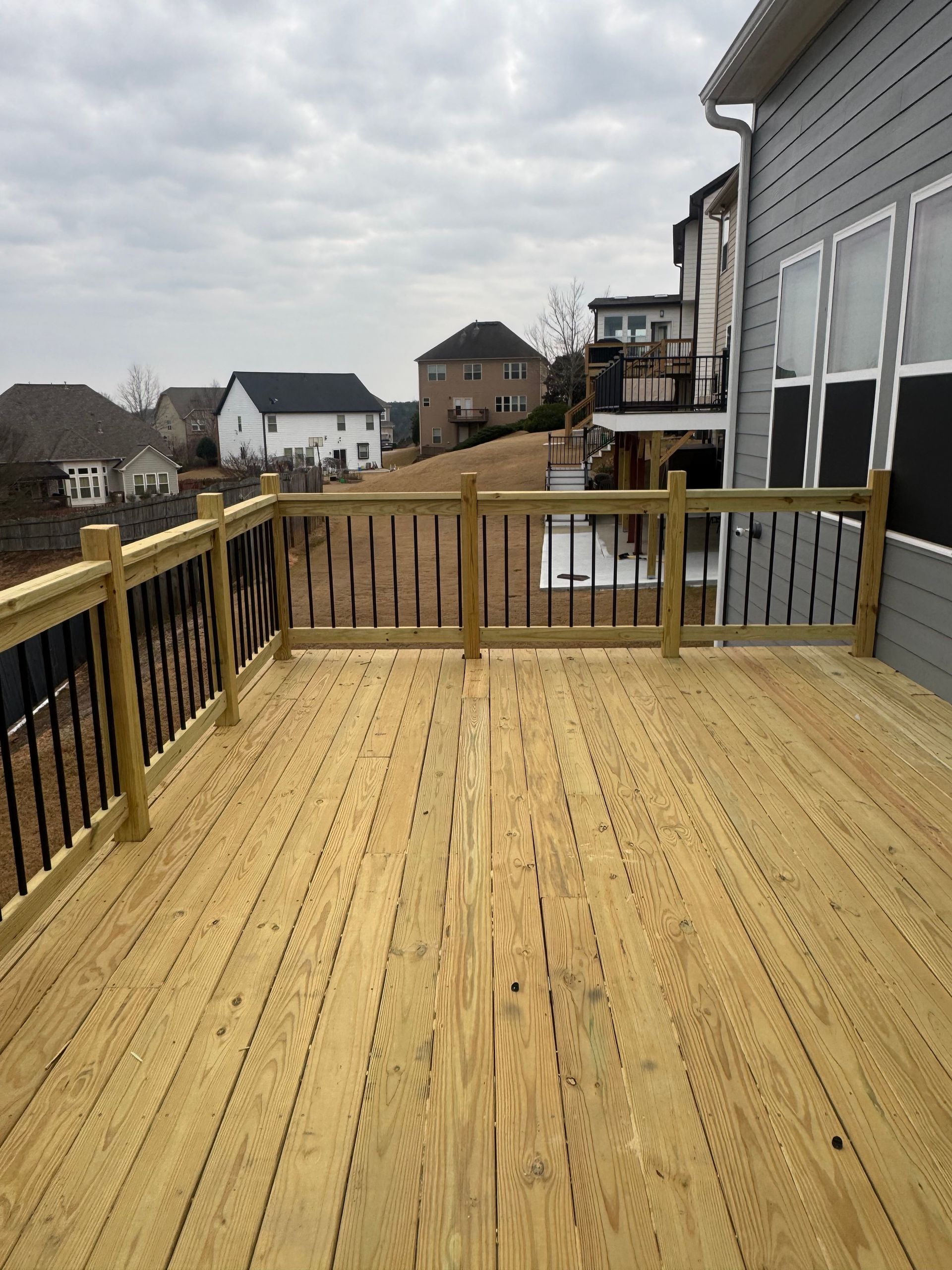 Wooden deck with railing beside a house, overlooking neighboring homes under a cloudy sky.