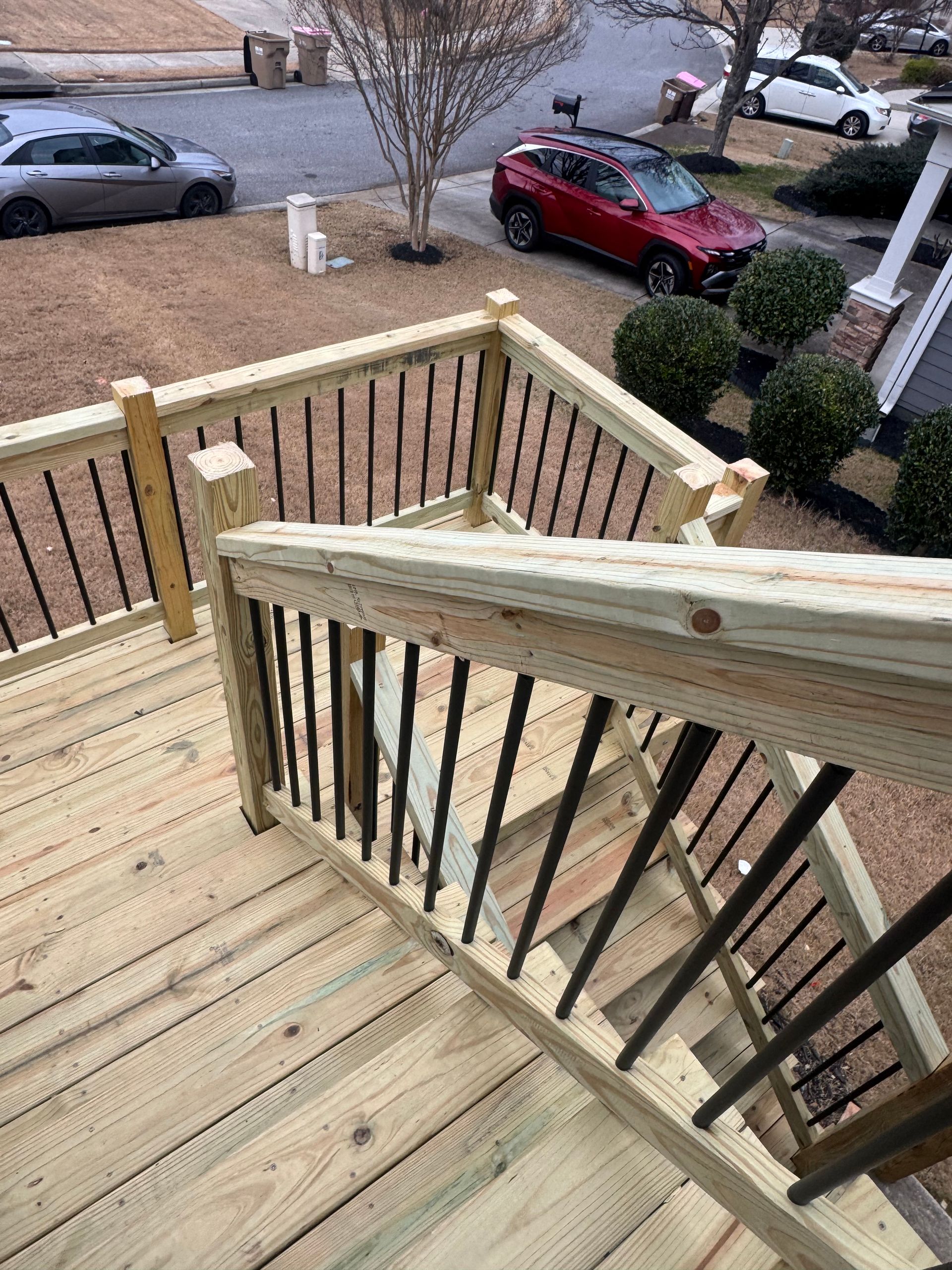 Wooden front porch stairs with black railings overlooking parked cars and a residential street