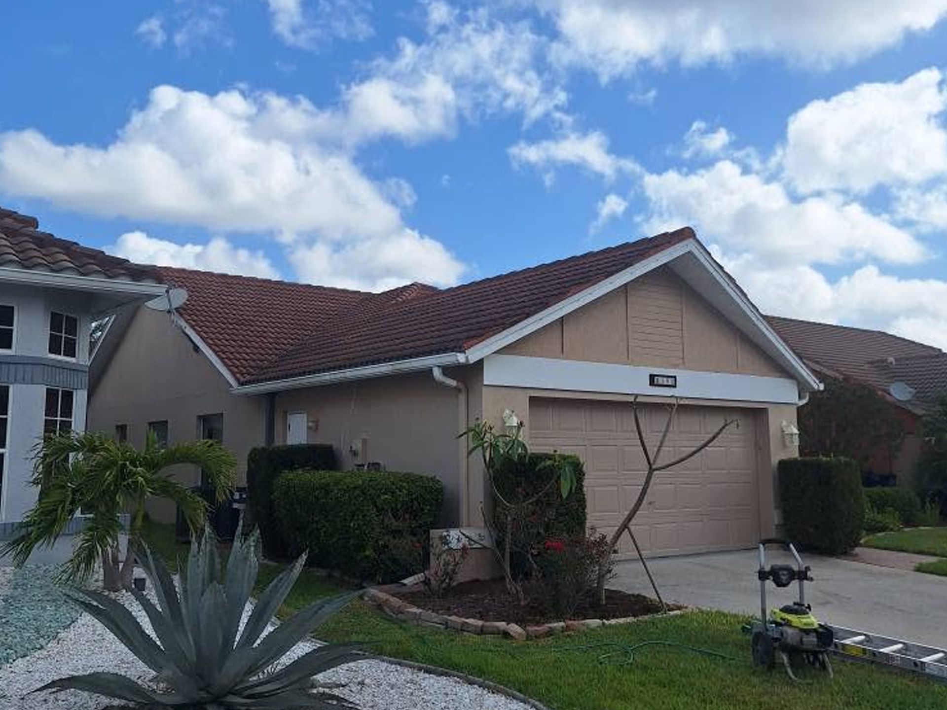 Suburban house with red tile roof, beige garage, and desert landscaping under a blue sky.