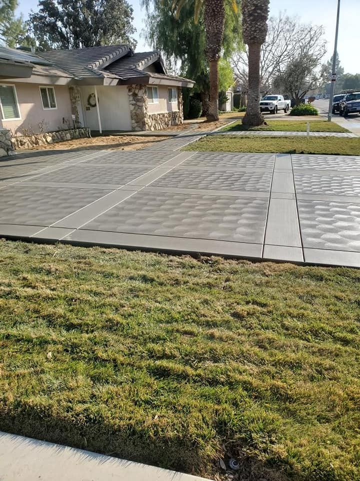 A concrete driveway with a lot of grass in front of a house.