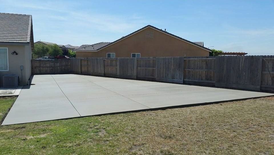 A concrete driveway leading to a house with a wooden fence.