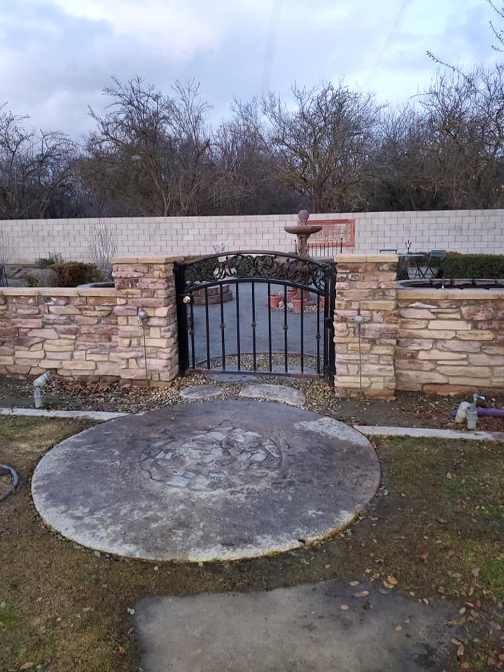 A metal gate is surrounded by a stone wall and a concrete circle.