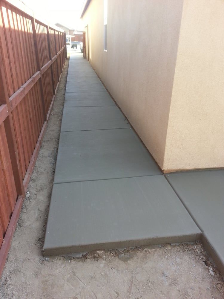 A concrete walkway next to a house with a wooden fence
