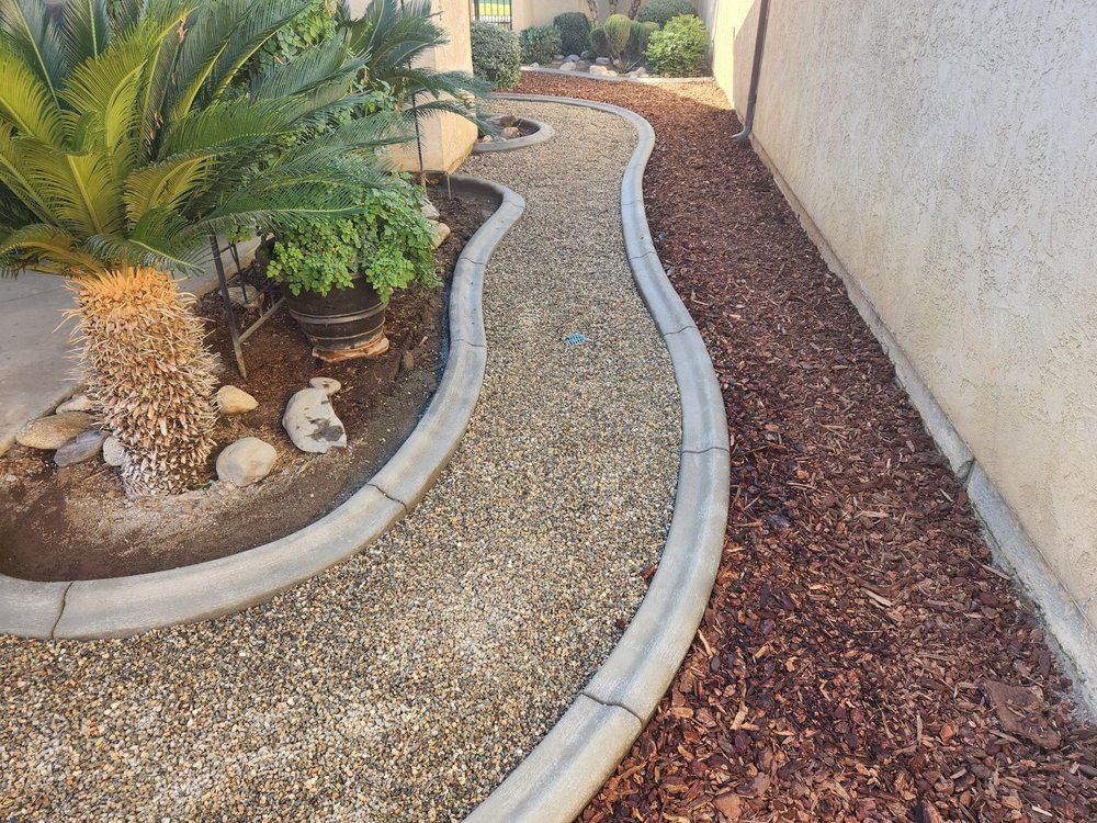 A concrete curb is surrounded by gravel and mulch in a garden.