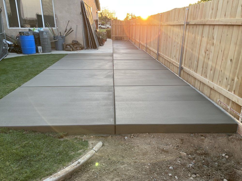 A concrete walkway is being built in a backyard next to a wooden fence.