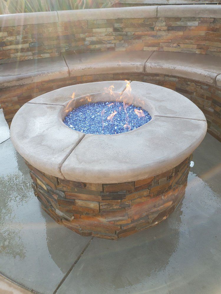 A fire pit with blue glass beads in it is sitting on a concrete surface.