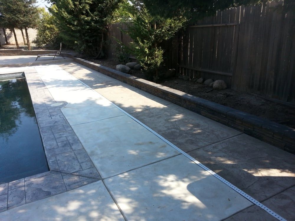 A concrete walkway next to a pool with a fence in the background