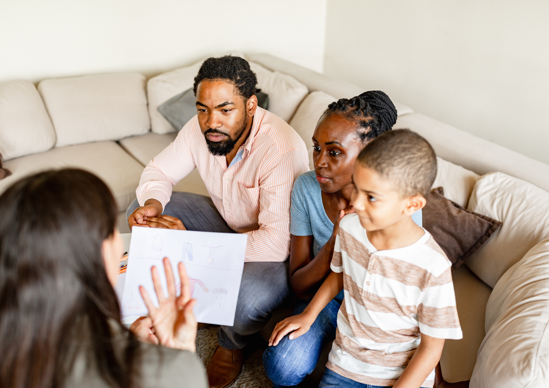 Family sitting on a couch, listening to a person holding papers during a discussion.