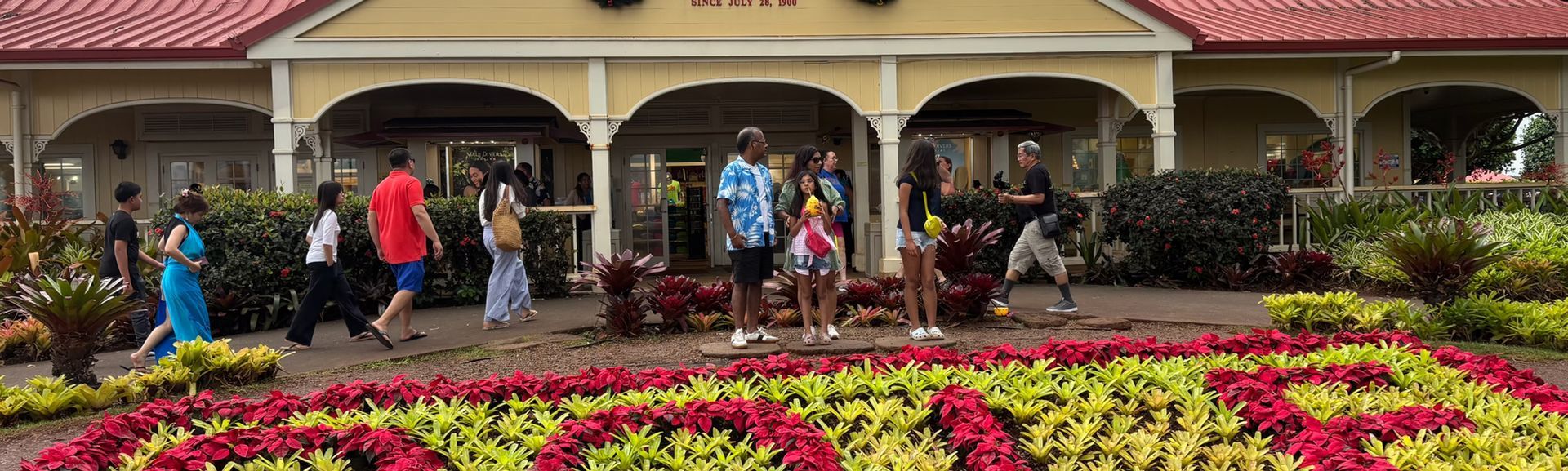 People walking in front of a flower bed and a building with arched porches
