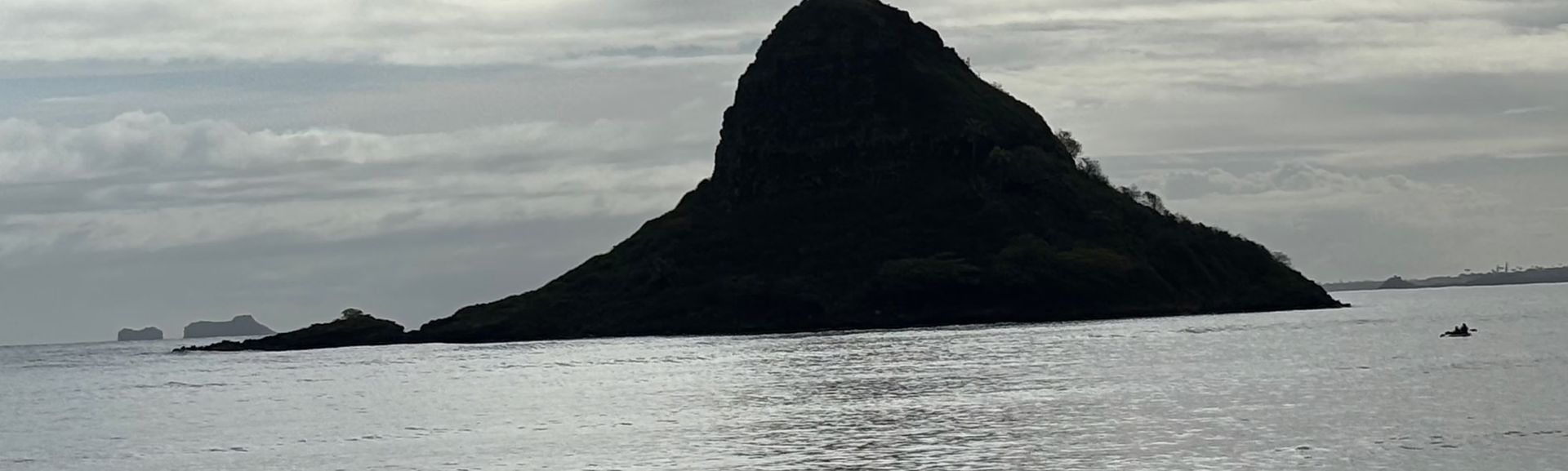 Dark, rocky island rising from a calm gray sea under an overcast sky