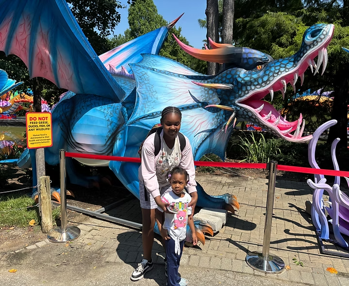 Man posing with a child in front of a large blue dragon sculpture outdoors