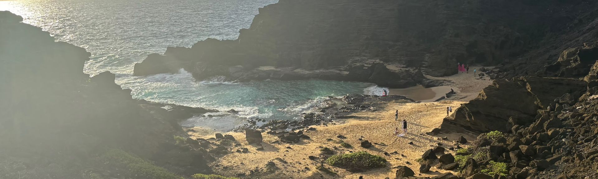Aerial view of a rocky coastline with waves, sandy beach, and cliffs in soft light
