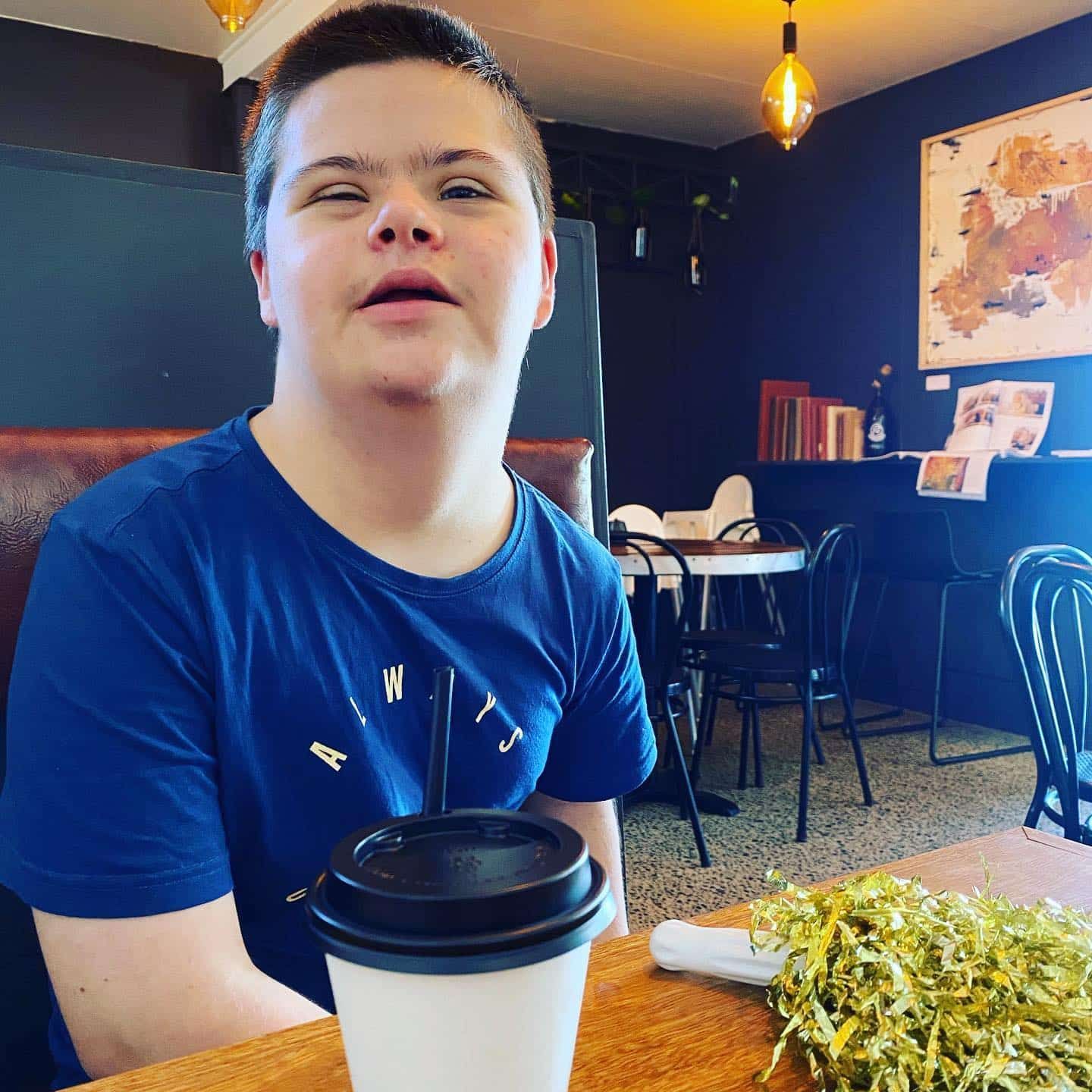 A Young Boy Is Sitting At A Table With A Cup Of Coffee — Tailored Support Services Pty Ltd In Maroochydore, QLD