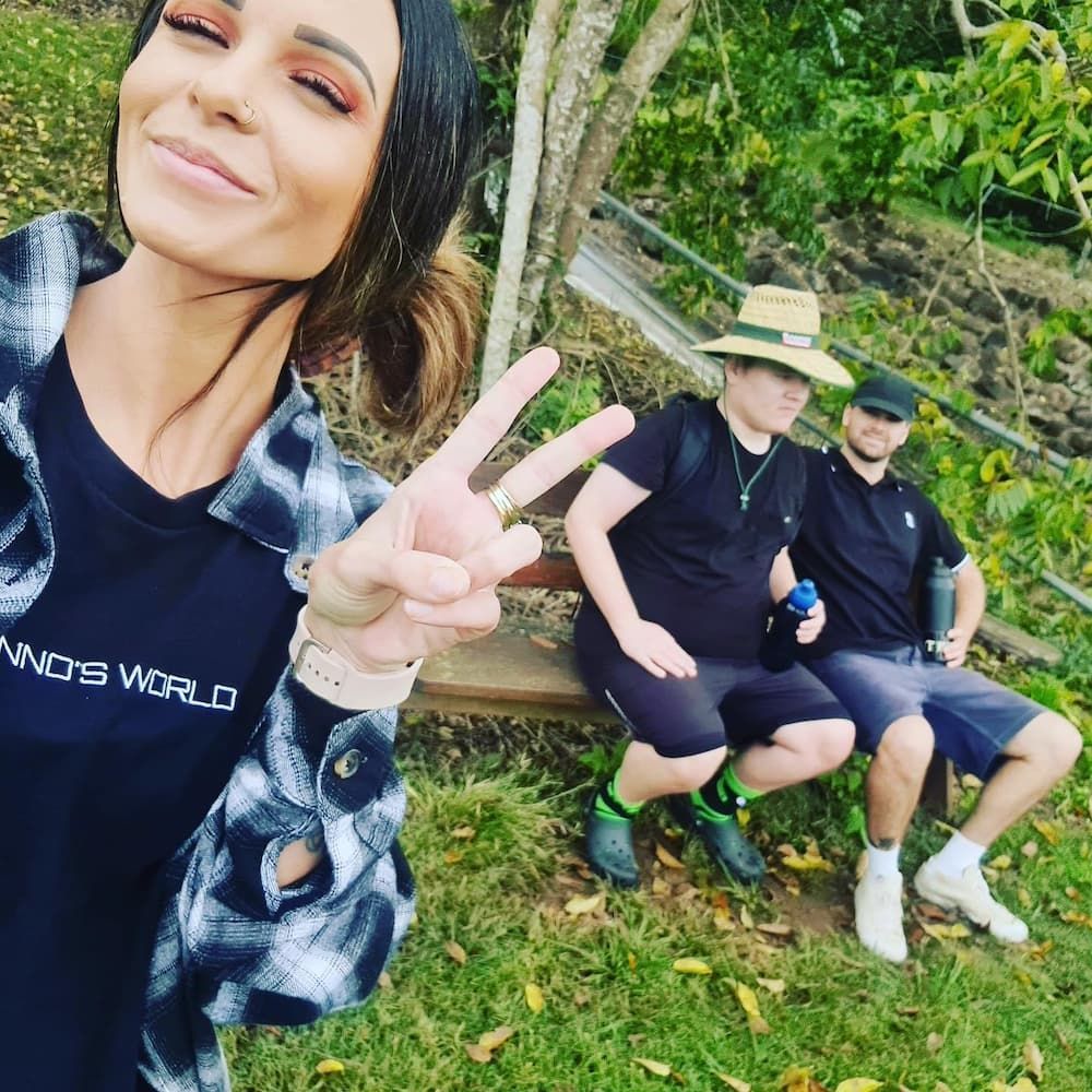 A Woman Is Giving A Peace Sign While Two Men Sit On A Bench — Tailored Support Services Pty Ltd In Maroochydore, QLD