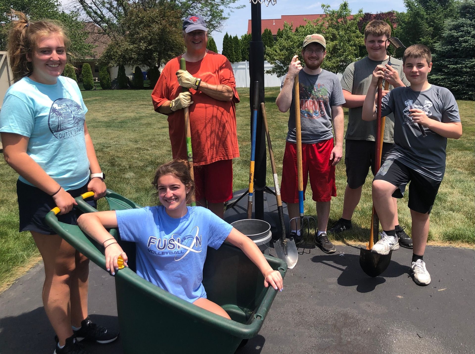 A girl in a blue shirt is sitting in a wheelbarrow