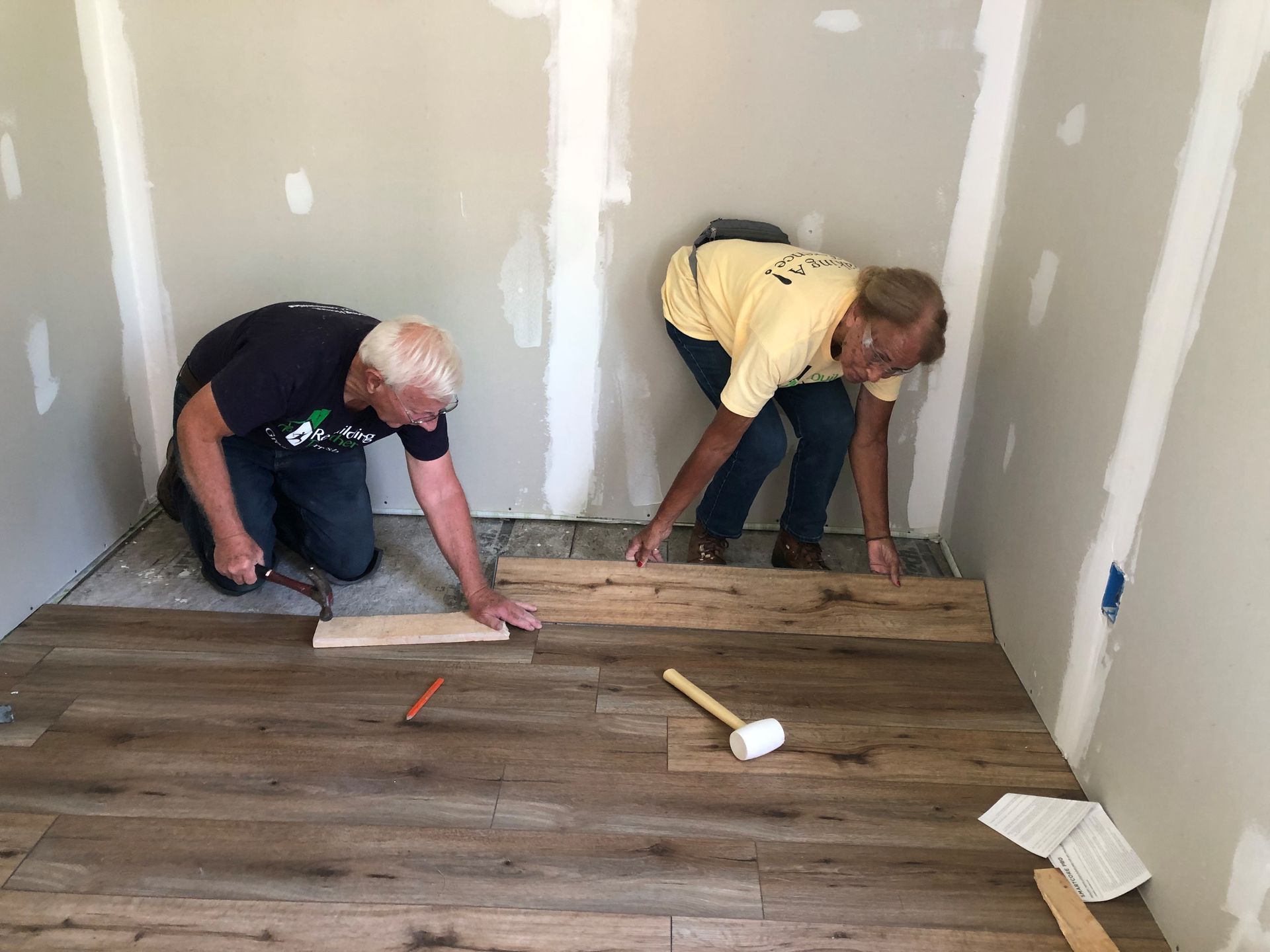 Two men installing wood flooring in a room with gray walls.