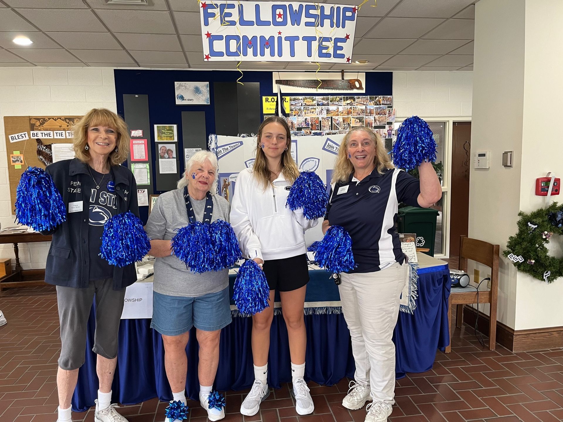 Four women holding pom poms in front of a sign that says fellowship committee