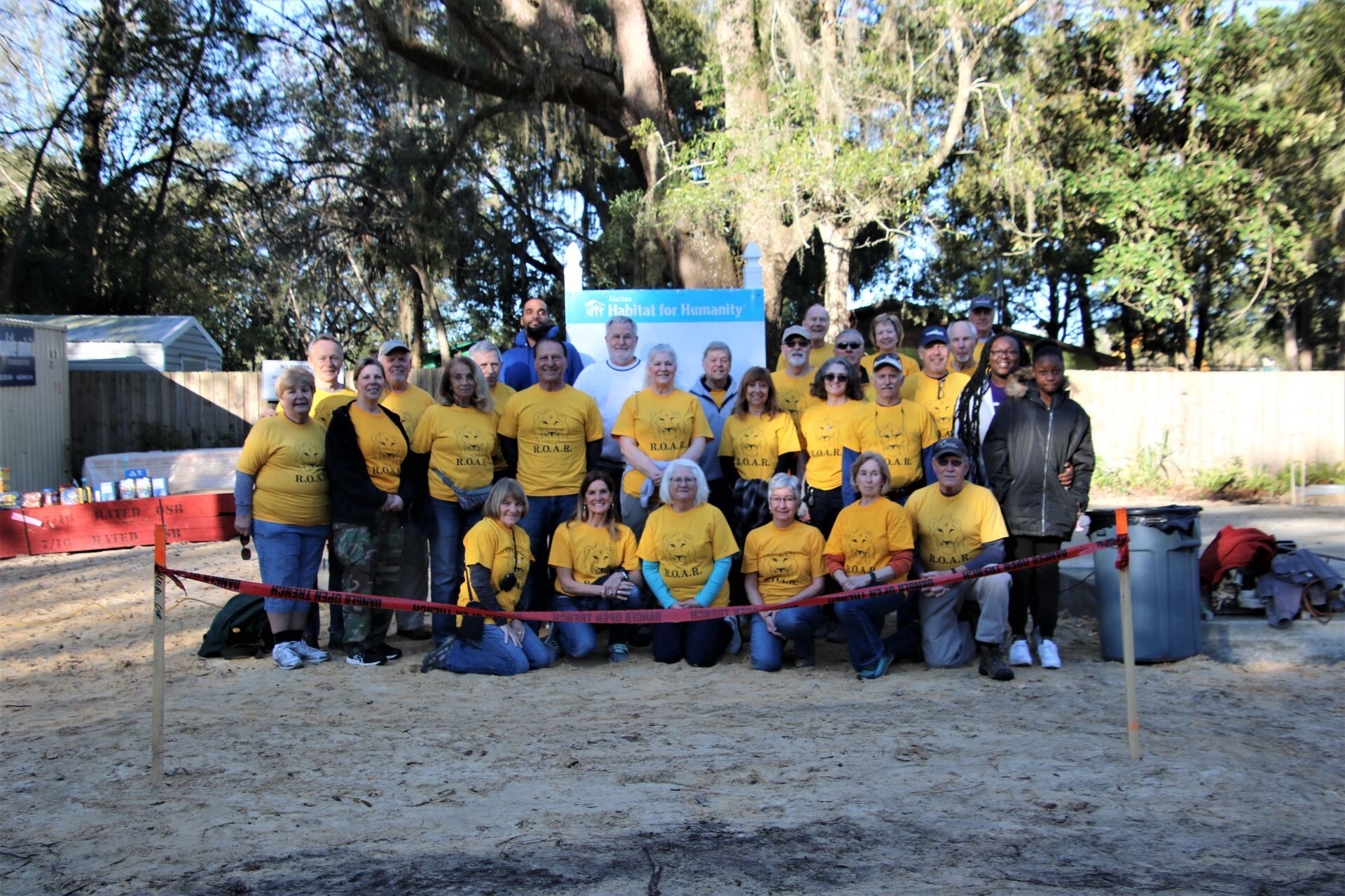 Group of people in yellow shirts at an outdoor event, smiling, posing near a sign.