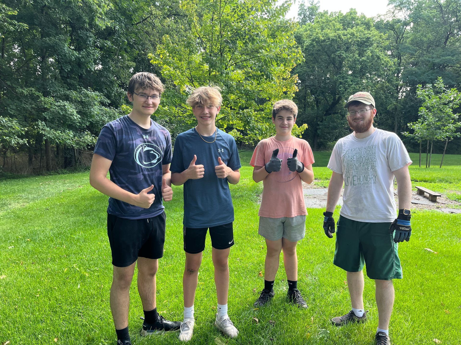 A group of young men are standing in the grass giving a thumbs up