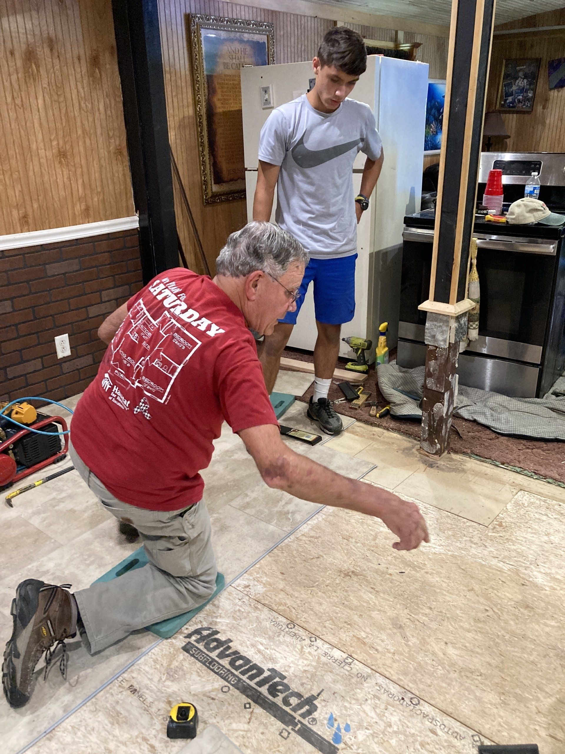 Man on knees, points at floor, another watches. Basement, construction, tools.