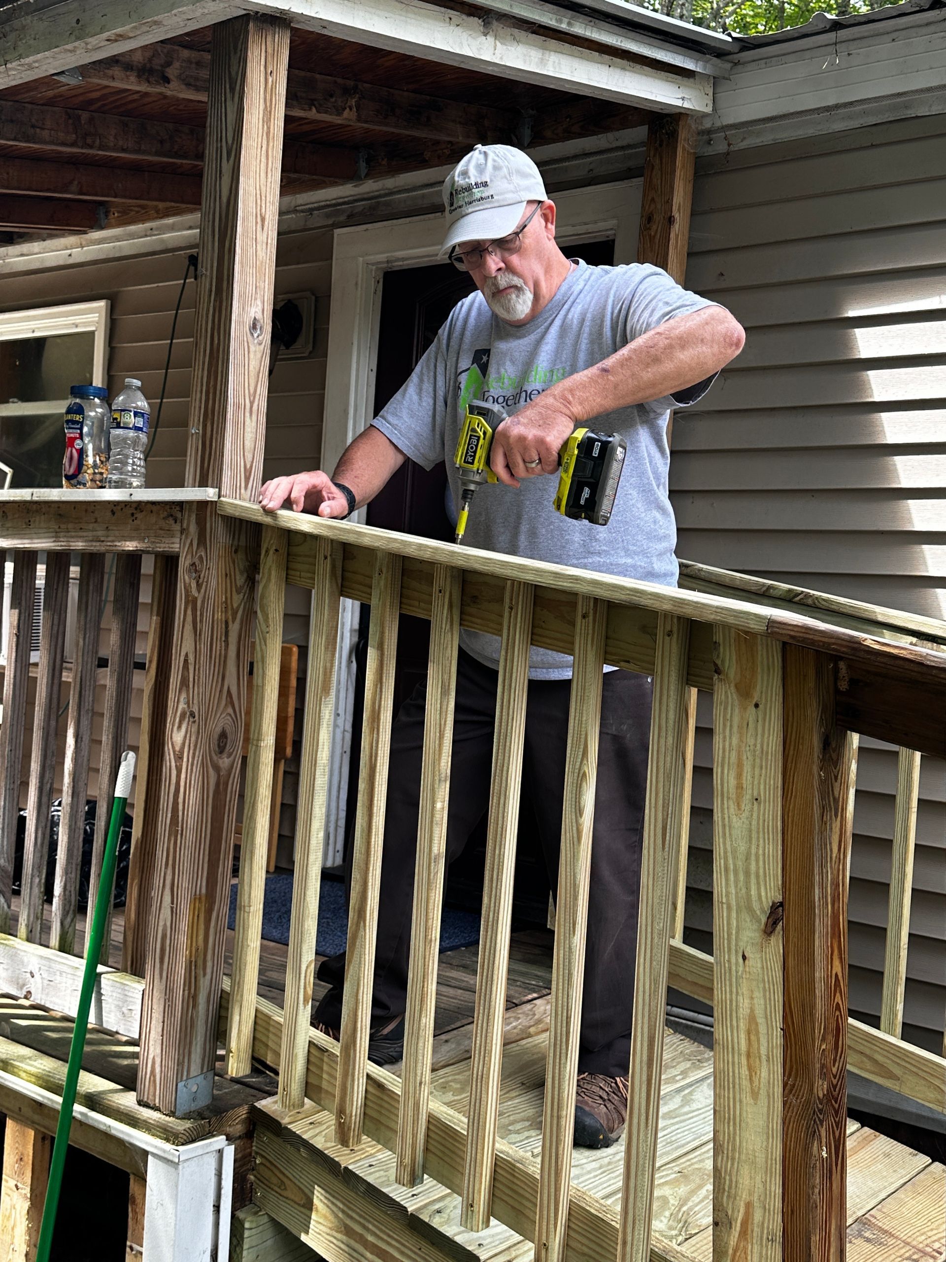 Man using a power drill to repair a wooden deck railing.