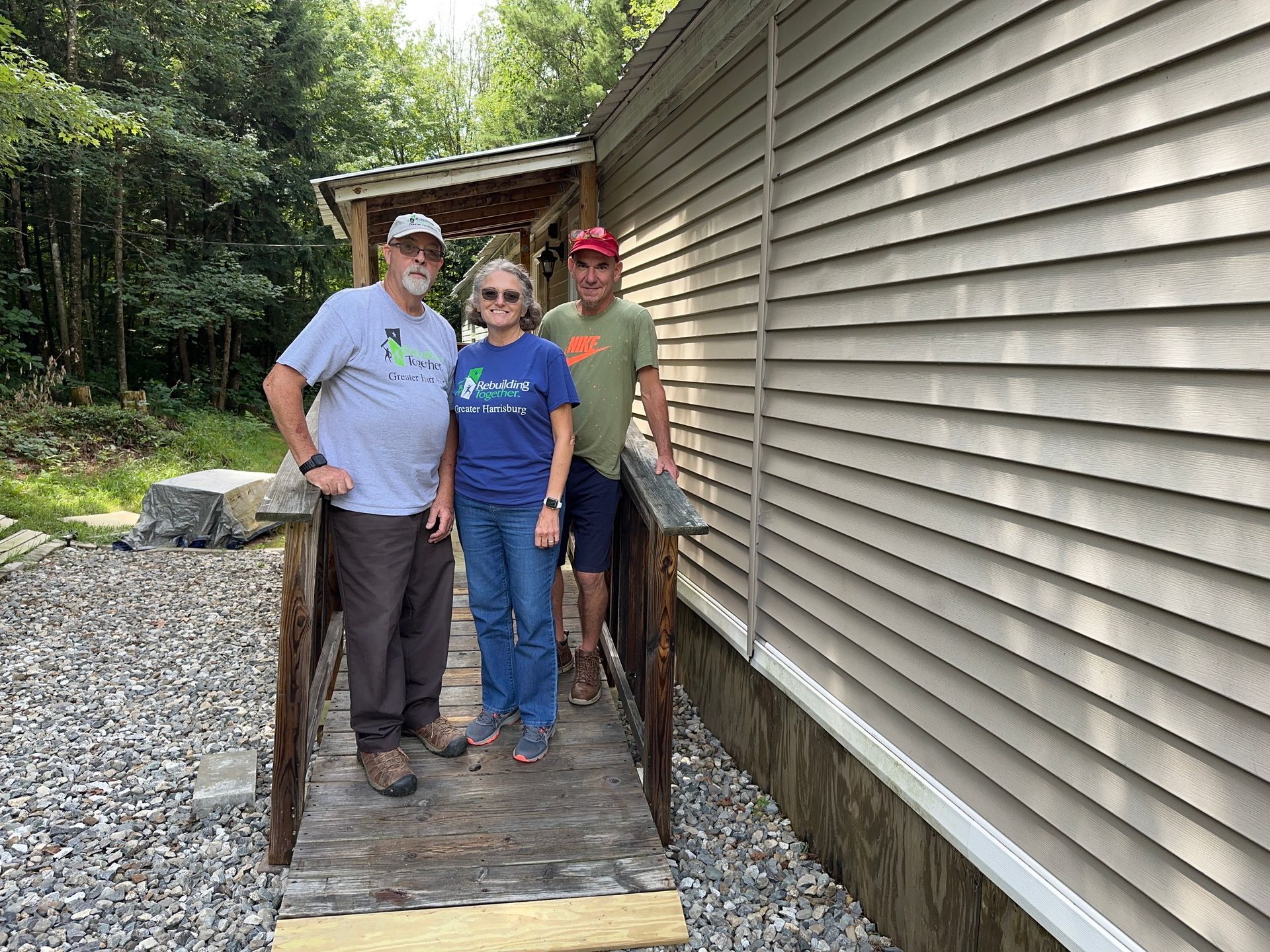 Three people stand on a wooden ramp next to a building with wood siding.