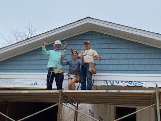 A group of people are standing on top of a scaffolding in front of a house.