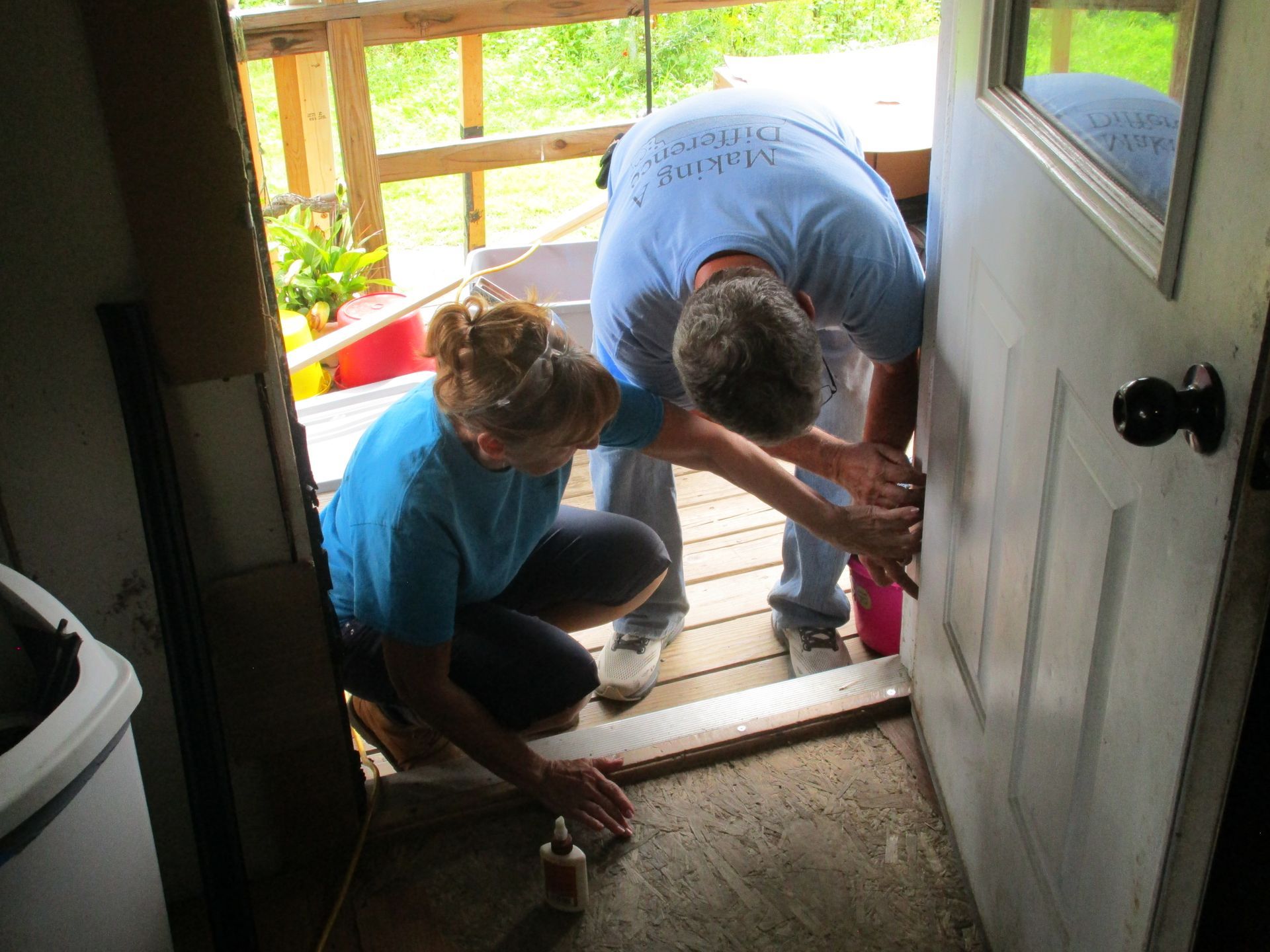 Two people, blue shirts, fixing a door. Interior shot, weathered entry.
