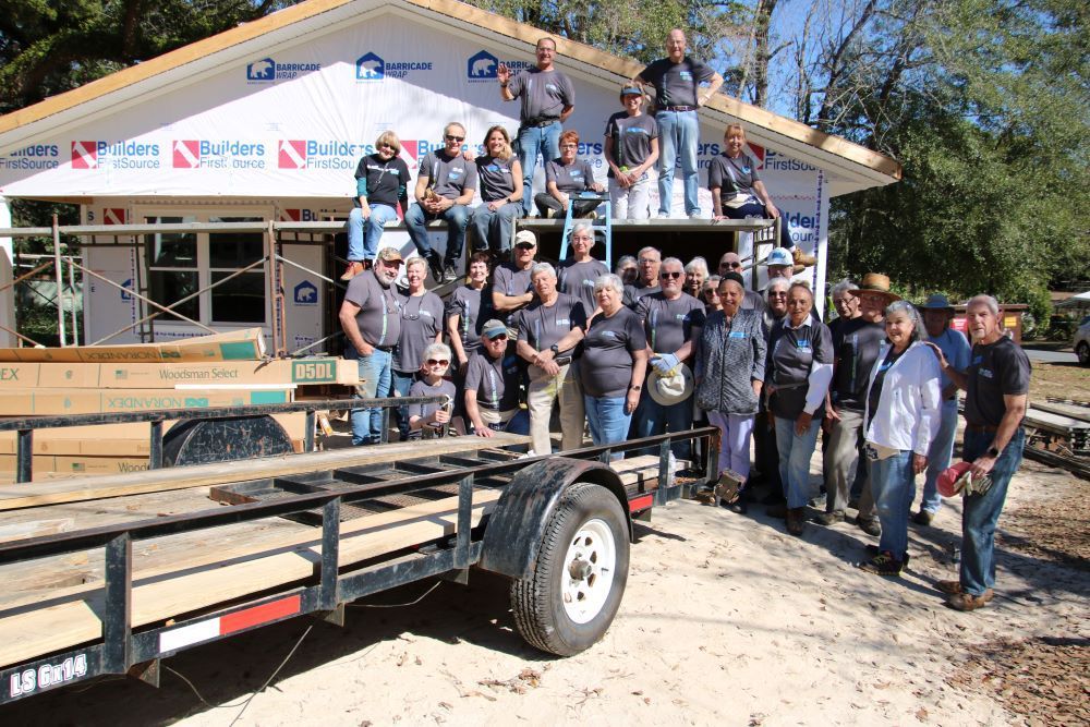 Group of volunteers posing on and around a partially built house; sunny day.