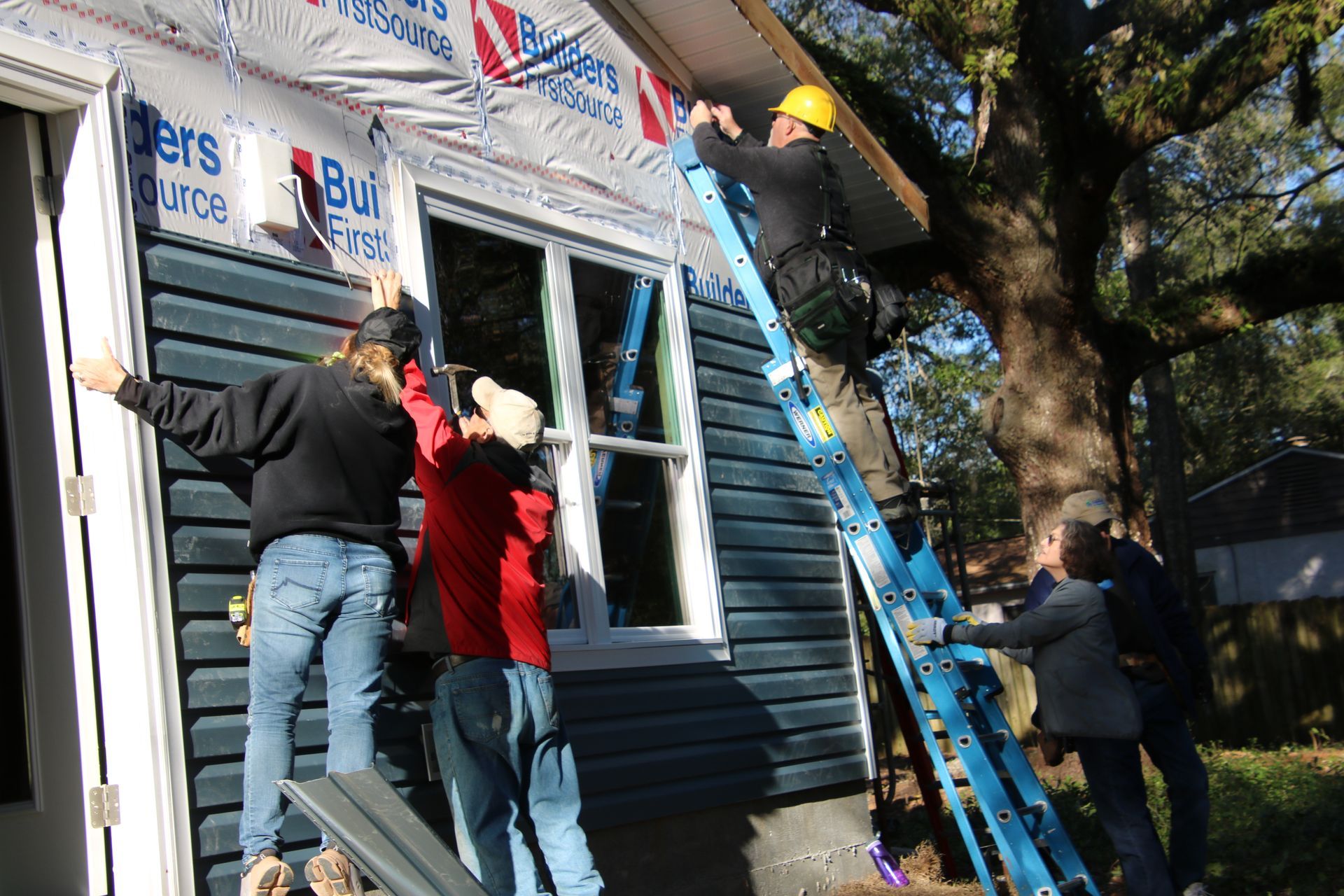 Construction workers installing trim on a blue house. One person on a blue ladder.
