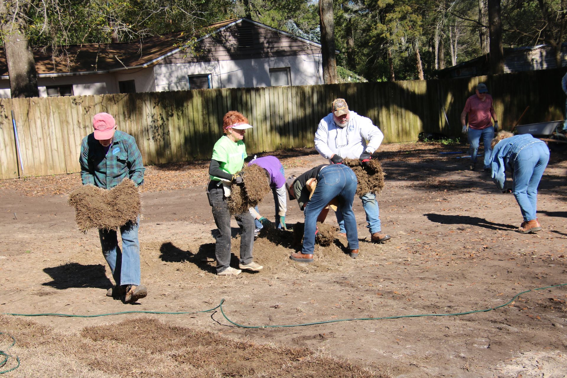 Group of people planting in an outdoor garden, wearing casual clothes.