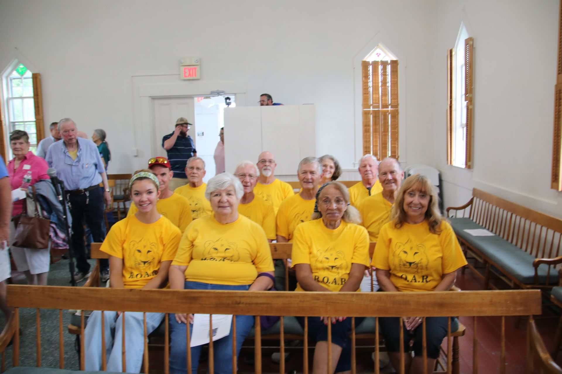 Group of people in yellow shirts, some with shaved heads, inside a building.