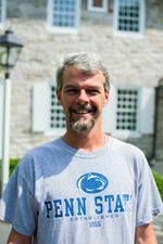 Man in Penn State t-shirt smiling in front of a stone building.