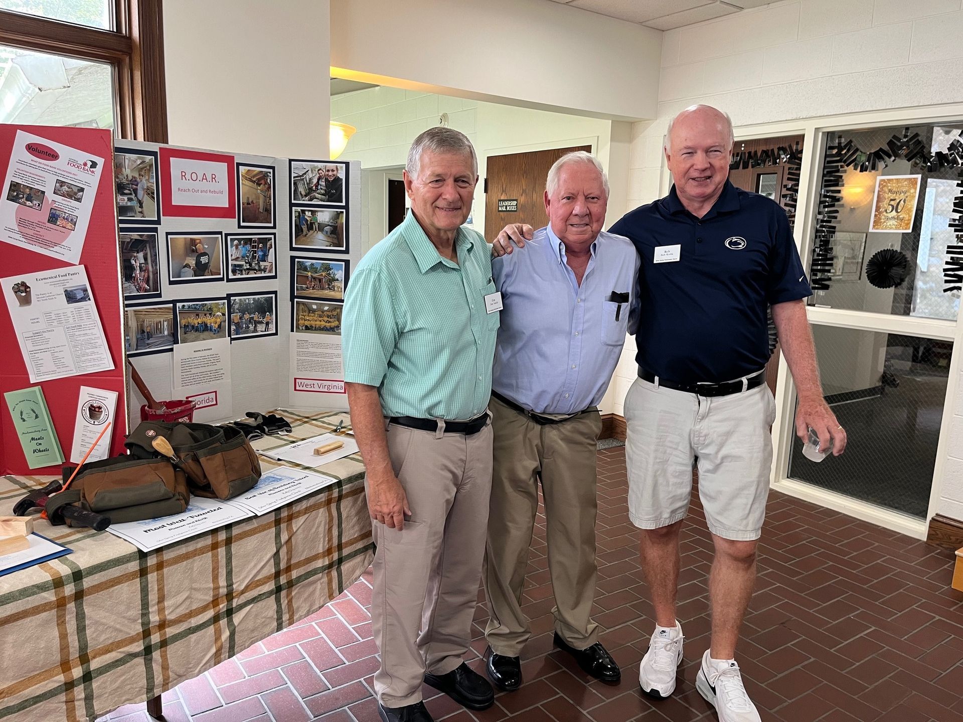 Three men are posing for a picture in front of a wall with pictures on it