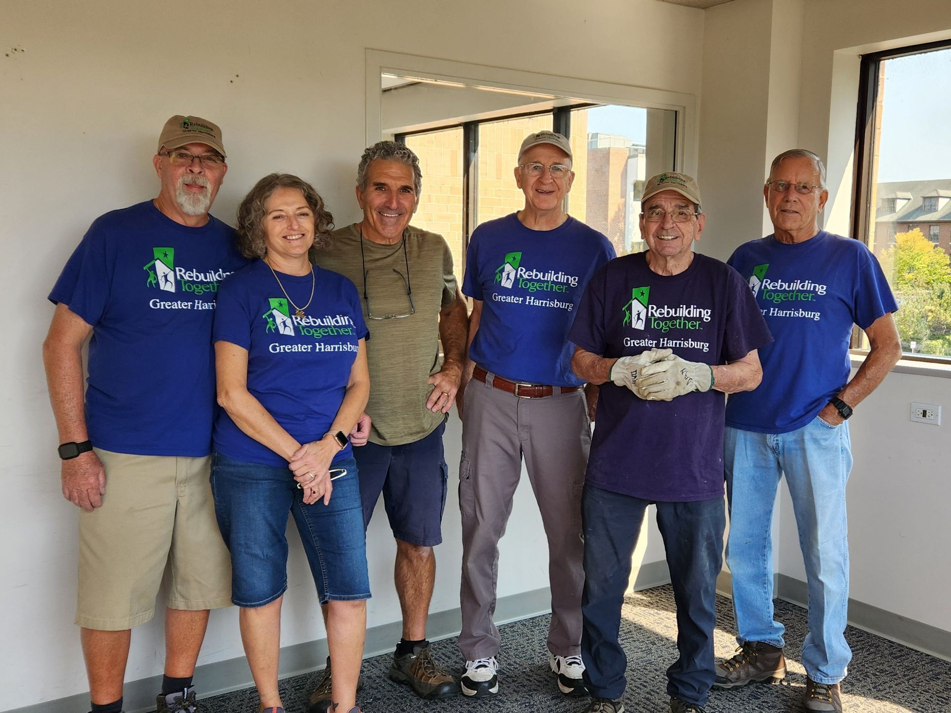 Six people, wearing matching t-shirts, pose indoors. Some wear hats.