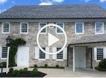 A large stone house with white shutters and a play button in front of it.