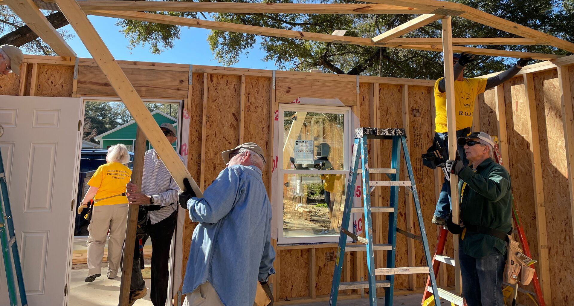 People building a wooden structure, indoors and outdoors. Men and women working together.