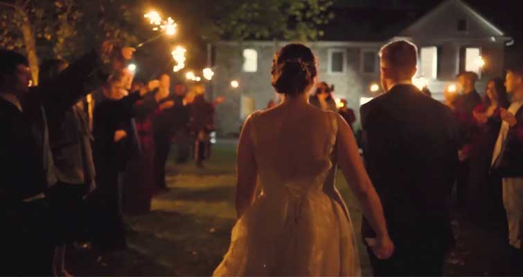 A bride and groom are walking through a crowd of people holding sparklers.